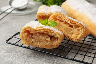 Photo of Tasty apple strudels with powdered sugar and mint on grey table, closeup