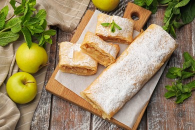 Photo of Tasty apple strudels with powdered sugar, mint and fruits on wooden table, flat lay