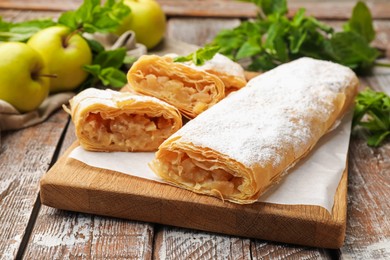 Photo of Tasty apple strudels with powdered sugar, mint and fruits on wooden table, closeup