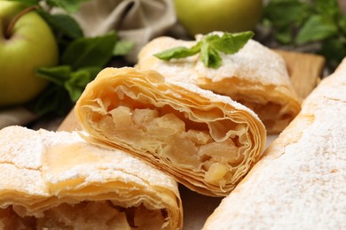Photo of Tasty apple strudels with powdered sugar, mint and fruits on table, closeup