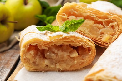 Photo of Tasty apple strudels with powdered sugar, mint and fruits on table, closeup