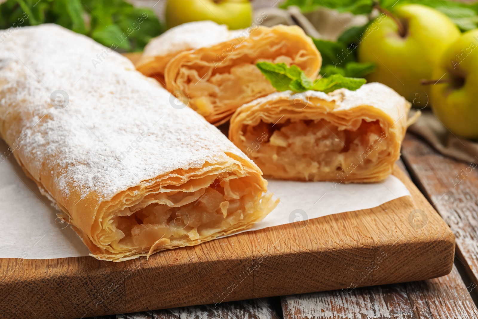 Tasty apple strudels with powdered sugar, mint and fruits on wooden table, closeup Photo of Tasty apple strudels with powdered sugar, mint and fruits on wooden table, closeup