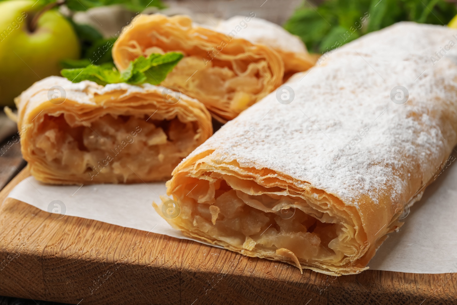 Tasty apple strudels with powdered sugar, mint and fruit on table, closeup Photo of Tasty apple strudels with powdered sugar, mint and fruit on table, closeup