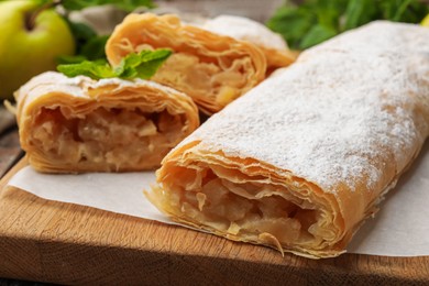 Photo of Tasty apple strudels with powdered sugar, mint and fruit on table, closeup