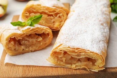 Photo of Tasty apple strudels with powdered sugar and mint on table, closeup
