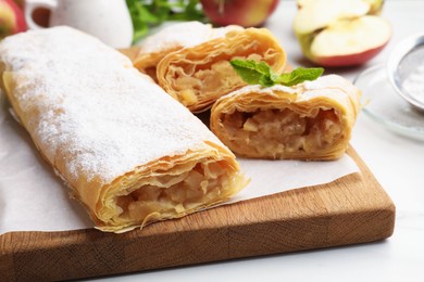Photo of Tasty apple strudels with powdered sugar and mint on white table, closeup