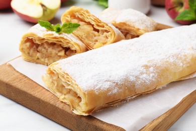 Photo of Tasty apple strudels with powdered sugar and mint on white table, closeup