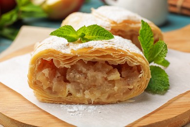 Photo of Pieces of tasty apple strudel with powdered sugar and mint on table, closeup