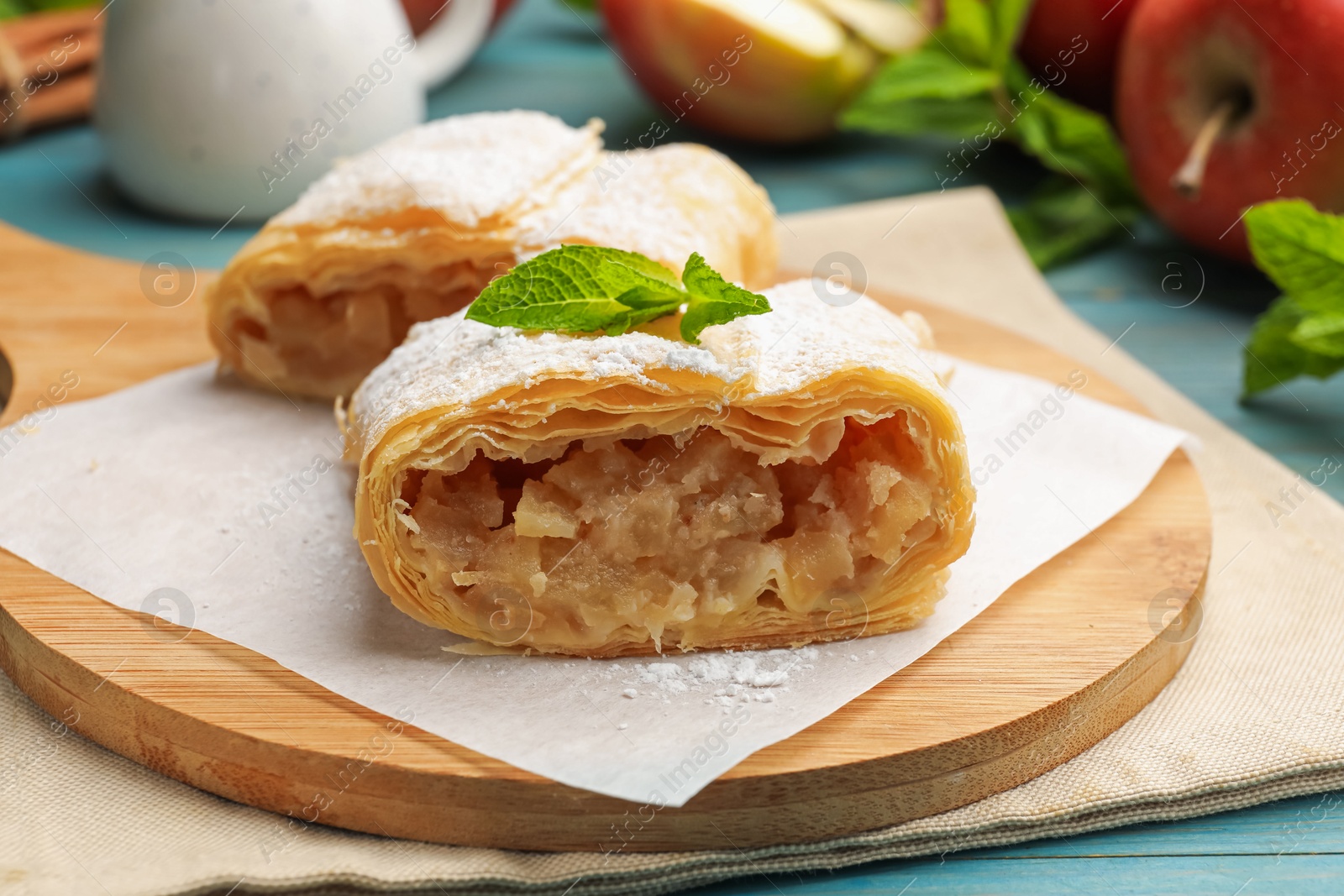 Pieces of tasty apple strudel with powdered sugar, mint and fruits on light blue wooden table, closeup Photo of Pieces of tasty apple strudel with powdered sugar, mint and fruits on light blue wooden table, closeup