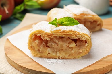Photo of Pieces of tasty apple strudel with powdered sugar and mint on table, closeup