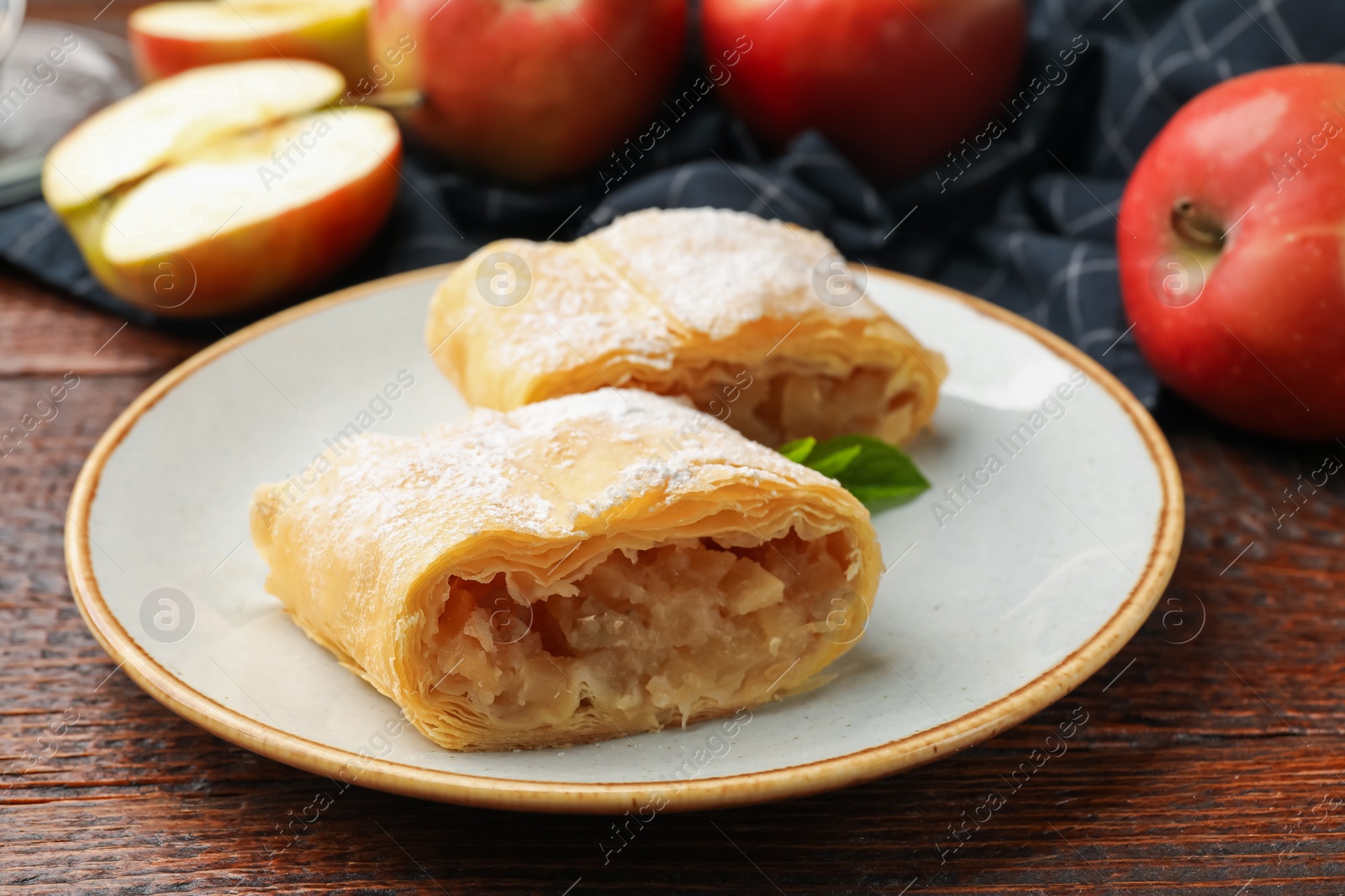 Pieces of tasty apple strudel with powdered sugar, mint and fruits on wooden table, closeup Photo of Pieces of tasty apple strudel with powdered sugar, mint and fruits on wooden table, closeup
