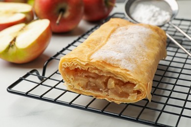 Photo of Tasty apple strudel with powdered sugar and fruits on white marble table, closeup
