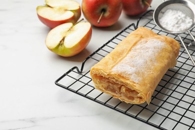 Photo of Tasty apple strudel with powdered sugar and fruits on white marble table, closeup. Space for text