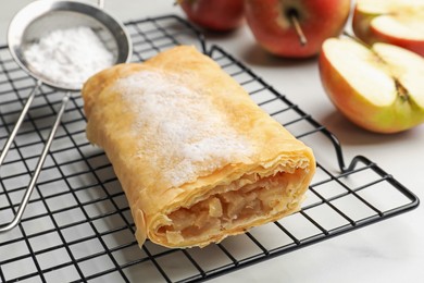 Photo of Tasty apple strudel with powdered sugar and fruits on white marble table, closeup