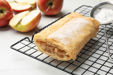 Photo of Tasty apple strudel with powdered sugar and fruits on white marble table, closeup