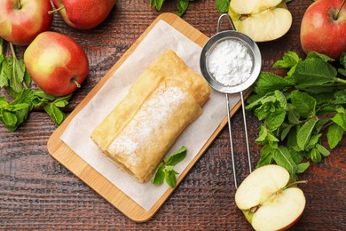Photo of Tasty apple strudel with powdered sugar, mint and fruits on wooden table, flat lay