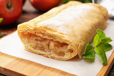 Photo of Tasty apple strudel with powdered sugar and mint on table, closeup