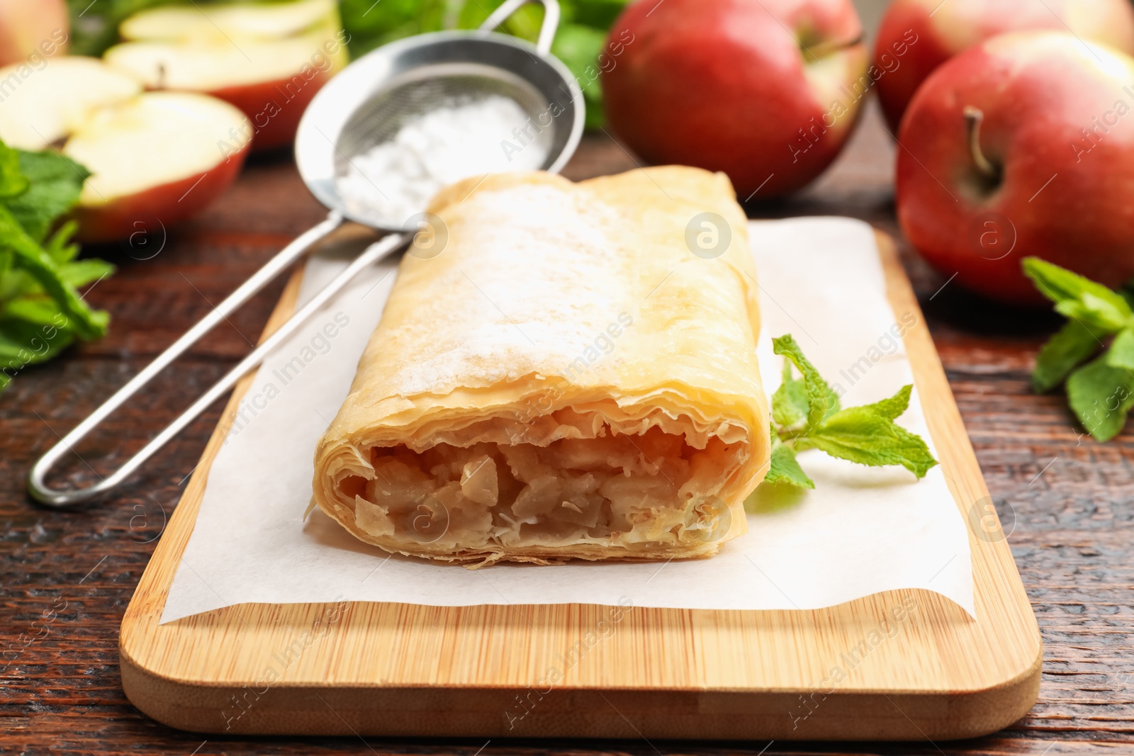 Tasty apple strudel with powdered sugar, mint and fruits on wooden table, closeup Photo of Tasty apple strudel with powdered sugar, mint and fruits on wooden table, closeup