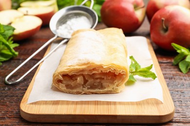 Photo of Tasty apple strudel with powdered sugar, mint and fruits on wooden table, closeup