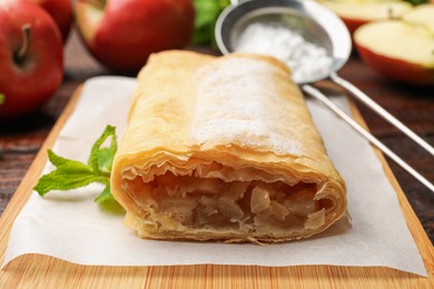 Photo of Tasty apple strudel with powdered sugar, mint and fruits on table, closeup