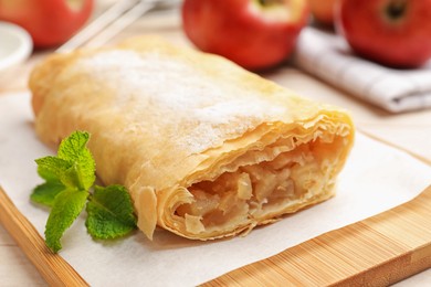 Photo of Tasty apple strudel with powdered sugar, mint and fruits on table, closeup