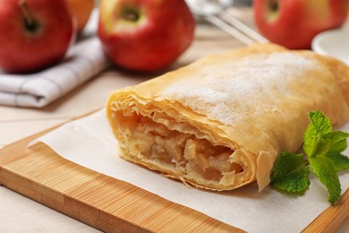 Photo of Tasty apple strudel with powdered sugar, mint and fruits on table, closeup