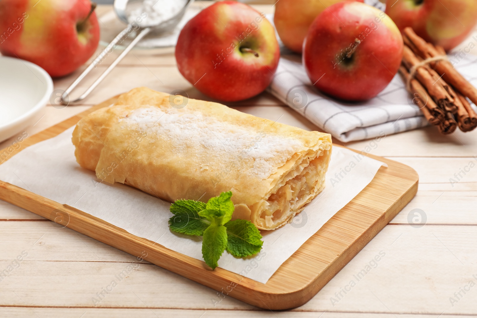 Tasty apple strudel with powdered sugar, mint, fruits and cinnamon on wooden table, closeup Photo of Tasty apple strudel with powdered sugar, mint, fruits and cinnamon on wooden table, closeup