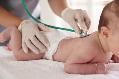 Photo of Pediatrician examining baby with stethoscope at table in clinic, closeup