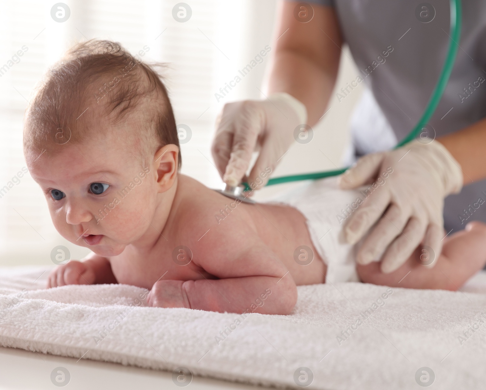 Pediatrician examining baby with stethoscope at table in clinic, closeup Photo of Pediatrician examining baby with stethoscope at table in clinic, closeup