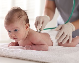 Photo of Pediatrician examining baby with stethoscope at table in clinic, closeup