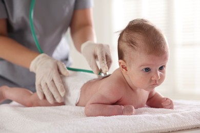 Photo of Pediatrician examining baby with stethoscope at table in clinic, closeup