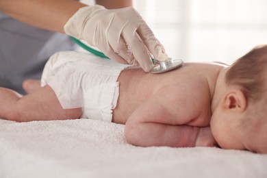 Photo of Pediatrician examining baby with stethoscope at table in clinic, closeup