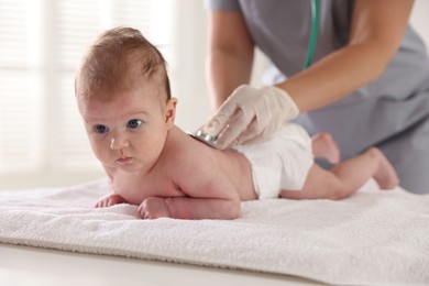 Photo of Pediatrician examining baby with stethoscope at table in clinic, closeup