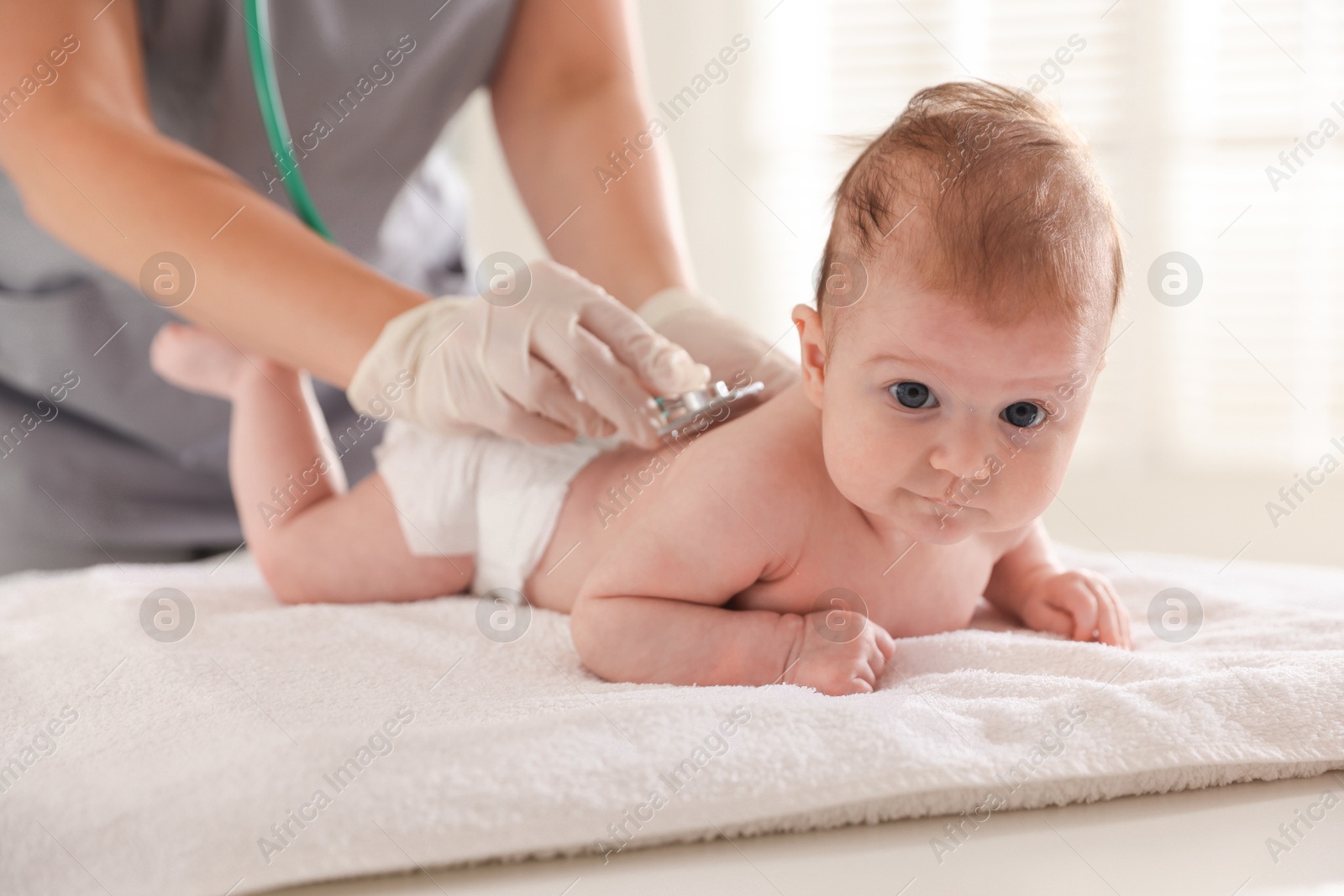 Pediatrician examining baby with stethoscope at table in clinic, closeup Photo of Pediatrician examining baby with stethoscope at table in clinic, closeup