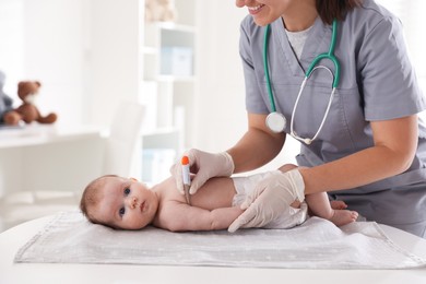 Photo of Pediatrician examining baby with thermometer at table in clinic, closeup
