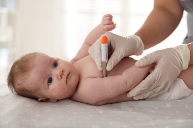 Photo of Pediatrician examining baby with thermometer at table in clinic, closeup