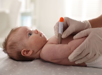 Photo of Pediatrician examining baby with thermometer at table in clinic, closeup