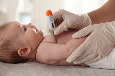 Photo of Pediatrician examining baby with thermometer at table in clinic, closeup