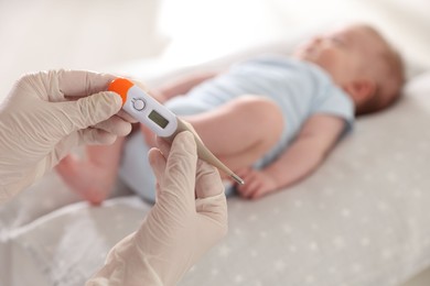 Photo of Pediatrician examining baby with thermometer in clinic, closeup