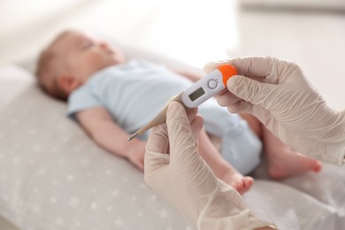 Photo of Pediatrician examining baby with thermometer in clinic, closeup