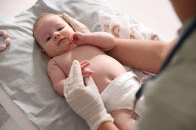 Photo of Pediatrician examining baby at table in clinic, closeup
