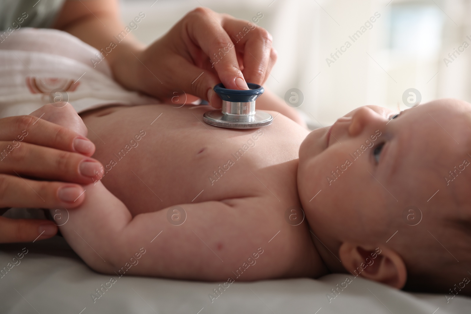 Pediatrician examining baby with stethoscope at table in clinic, closeup Photo of Pediatrician examining baby with stethoscope at table in clinic, closeup