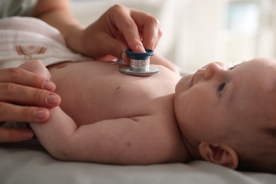 Photo of Pediatrician examining baby with stethoscope at table in clinic, closeup