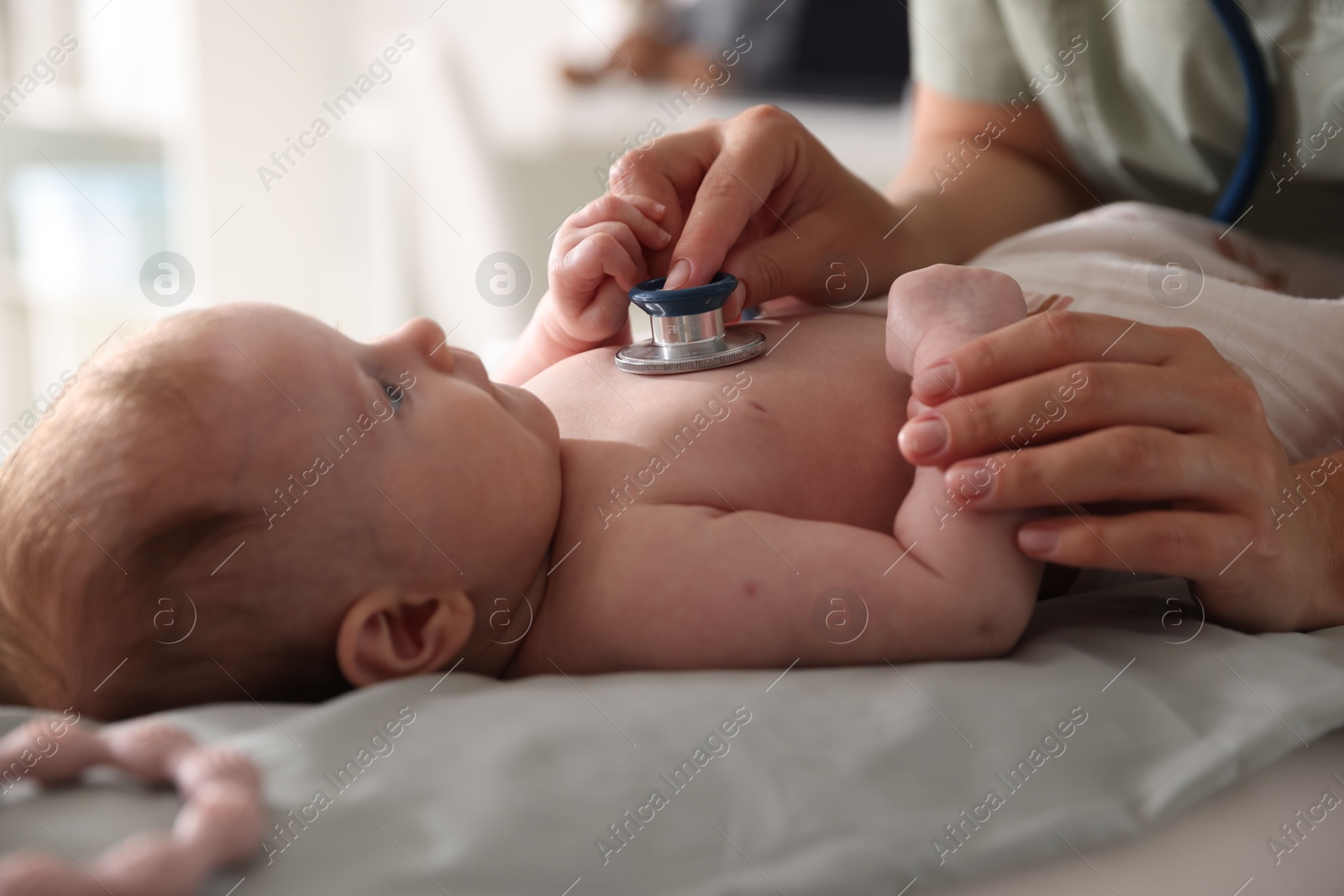 Pediatrician examining baby with stethoscope at table in clinic, closeup Photo of Pediatrician examining baby with stethoscope at table in clinic, closeup