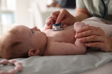 Photo of Pediatrician examining baby with stethoscope at table in clinic, closeup