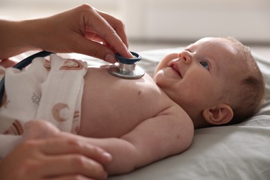 Photo of Pediatrician examining baby with stethoscope at table in clinic, closeup
