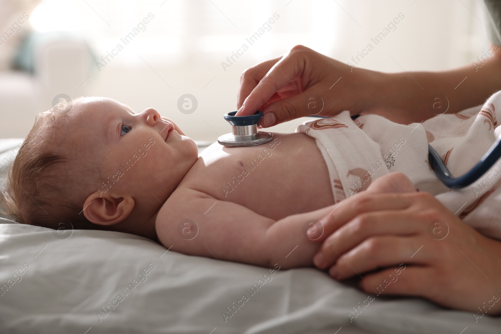 Pediatrician examining baby with stethoscope at table in clinic, closeup Photo of Pediatrician examining baby with stethoscope at table in clinic, closeup