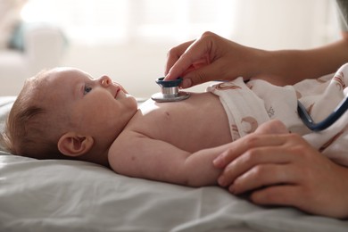 Photo of Pediatrician examining baby with stethoscope at table in clinic, closeup