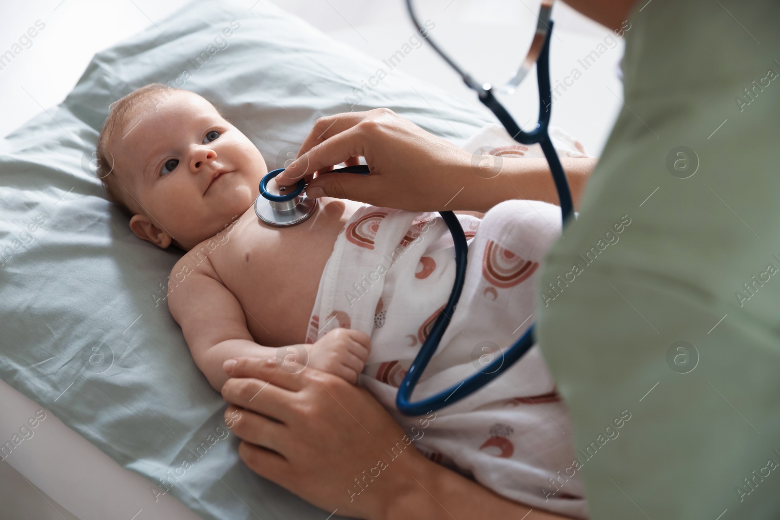Pediatrician examining baby with stethoscope at table in clinic, closeup Photo of Pediatrician examining baby with stethoscope at table in clinic, closeup