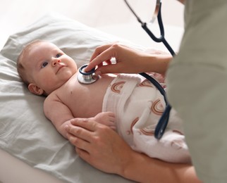 Photo of Pediatrician examining baby with stethoscope at table in clinic, closeup